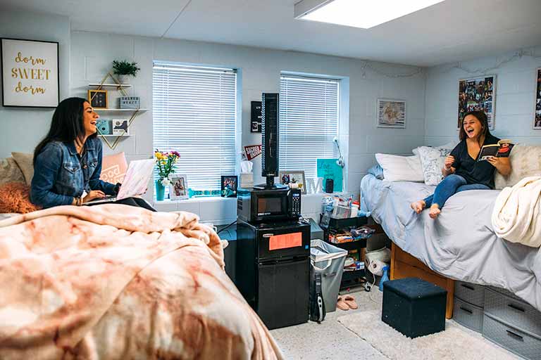 Two students laugh in their dorm room.