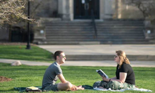 two students studying together on the lawn in front of a limestone building at Illinois Wesleyan University